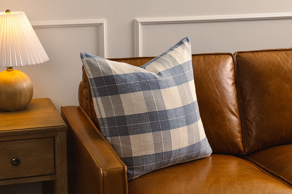 A blue and cream plaid pillow on an orange leather couch.