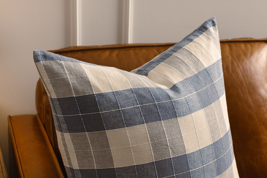 A blue and cream plaid pillow on an orange leather couch.