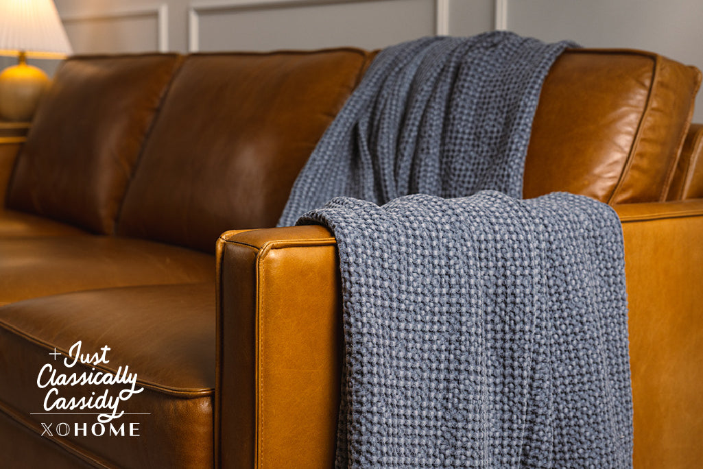 A dusty blue waffle weave throw on an orange leather couch.