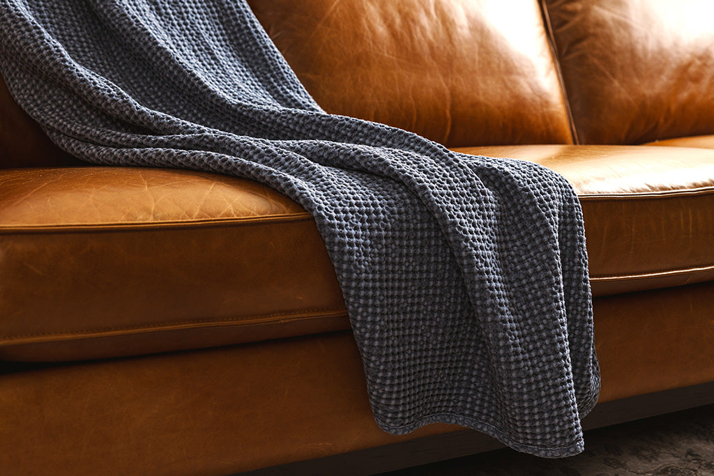 A dusty blue waffle weave throw on an orange leather couch.