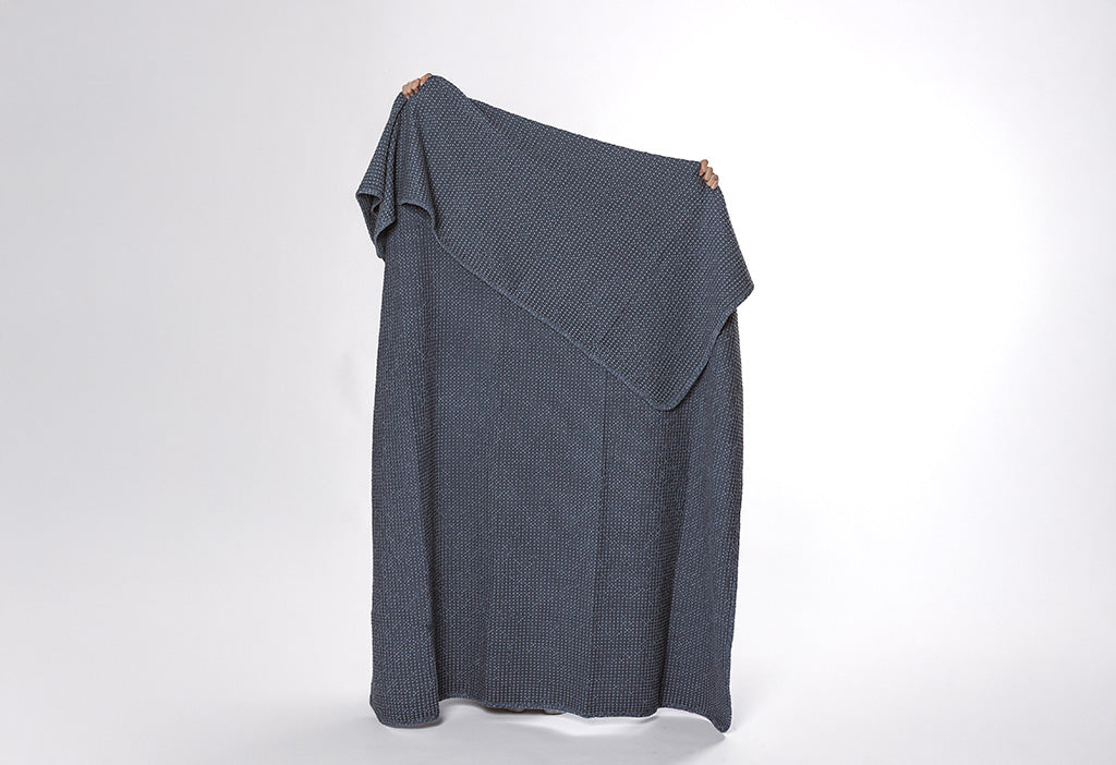 A dusty blue waffle weave blanket on a white backdrop.