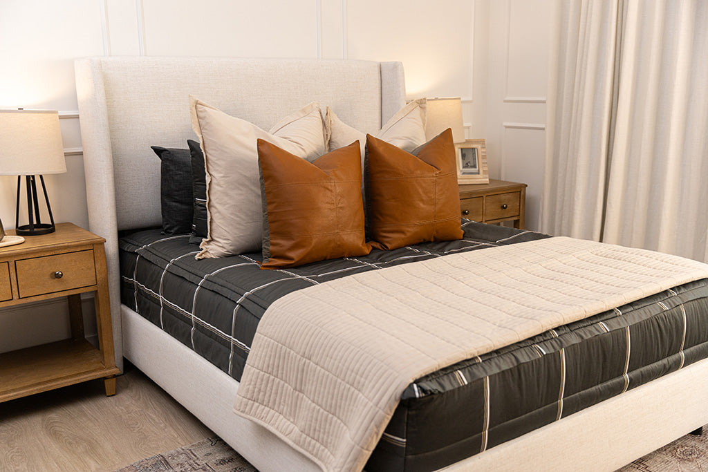 Charcoal with white and brown grid pattern bedding with tan and brown pillows and tan patterned blanket.