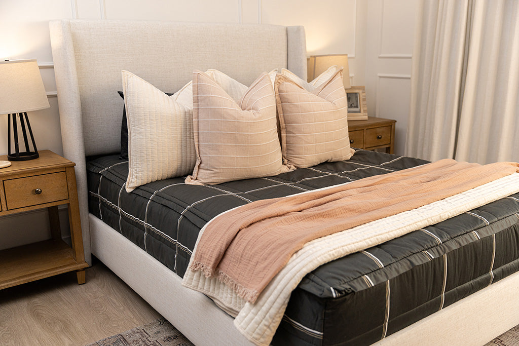 Charcoal with white and brown grid pattern bedding with pink and cream pillows and blankets.