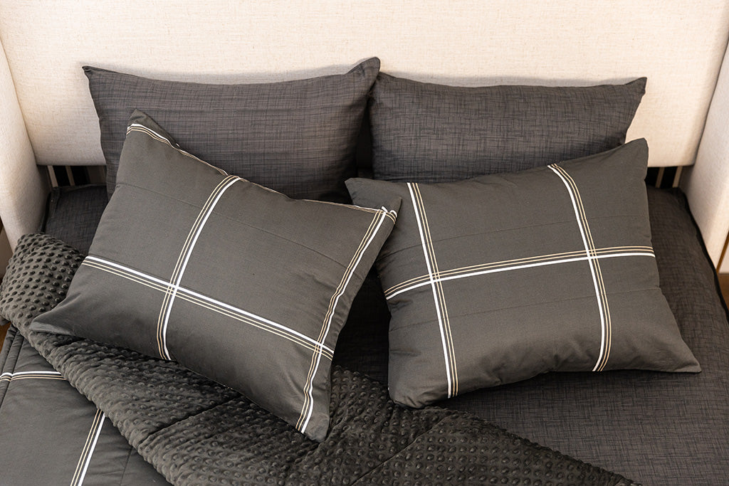 A queen bed made with black plaid zipper bedding with the top portion unzipped and slightly pulled back and four pillows arranged on top