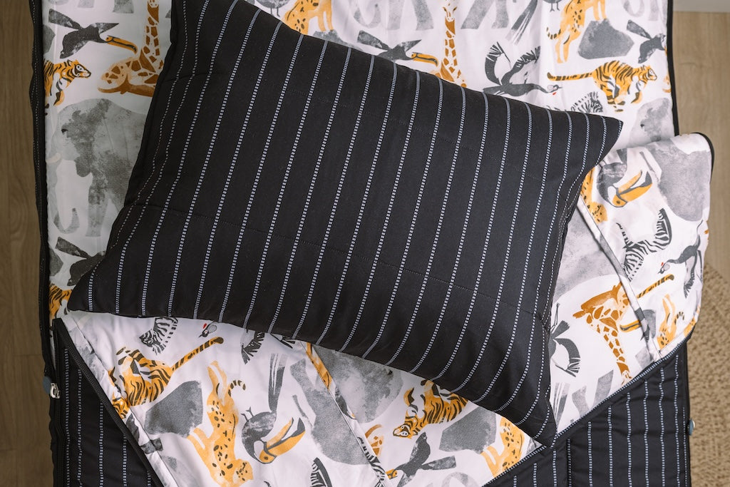 Black and jungle printed kids zipper bedding with the top unzipped and one side pulled back to reveal the inside lining, the pillow tossed on top of the bed.