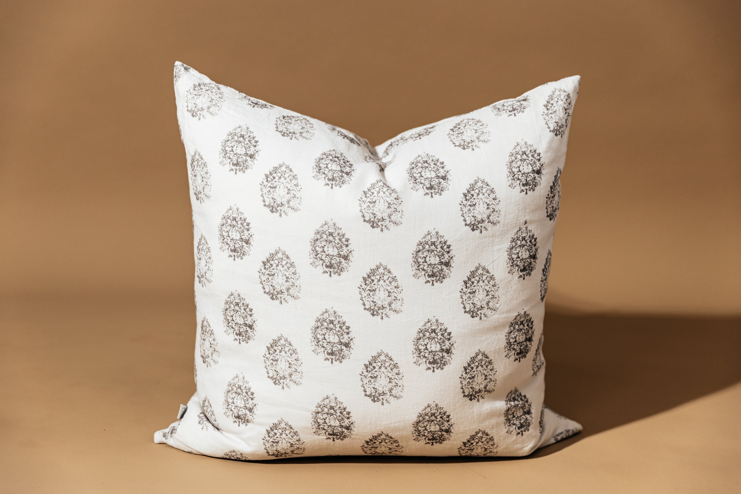 A charcoal floral print white pillow arranged on a brown background.