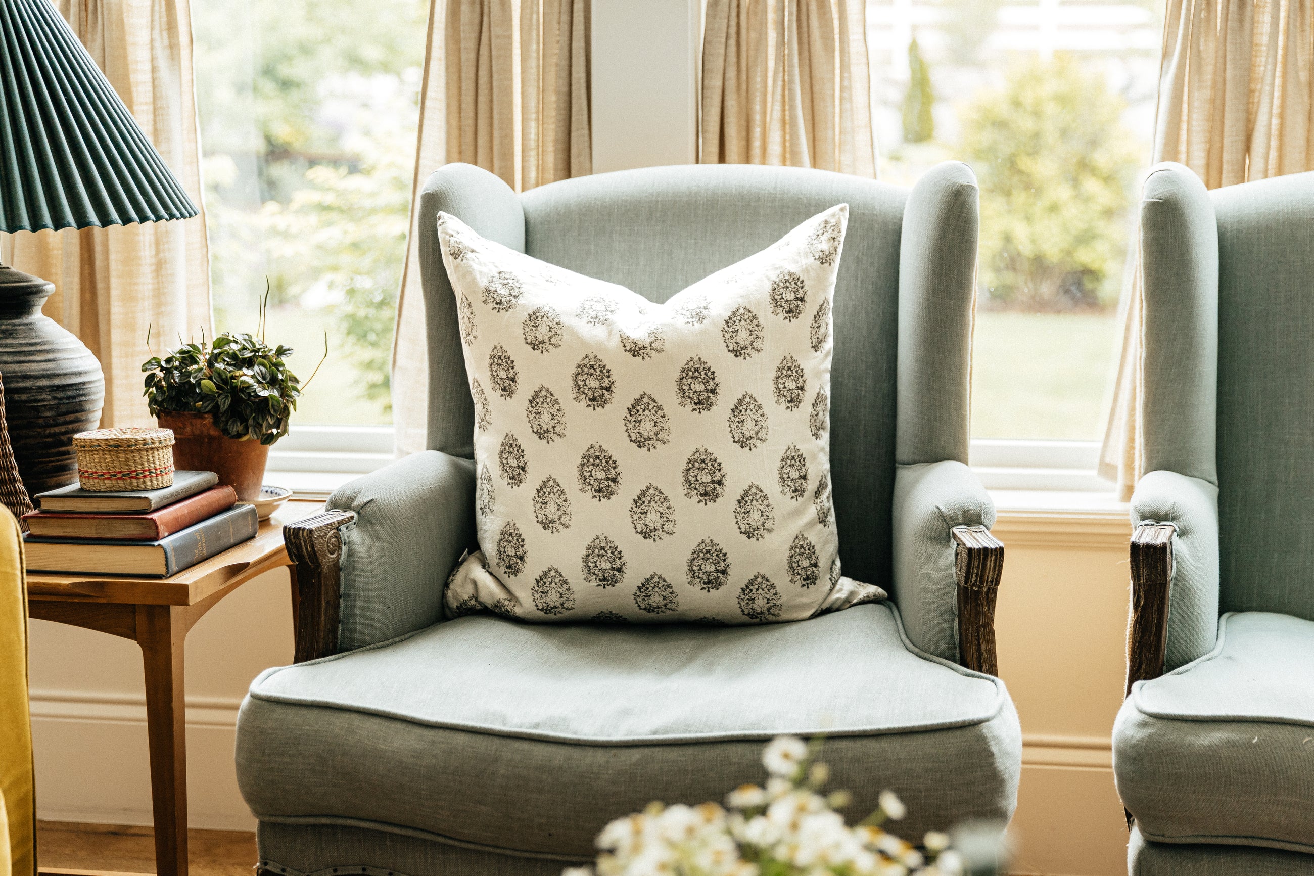 A charcoal floral print white pillow arranged on a light blue fabric antique chair.