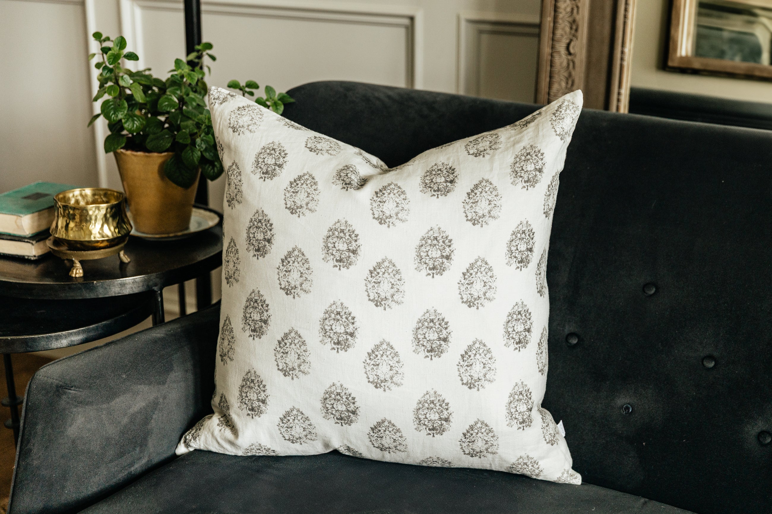 A charcoal floral print white pillow arranged on a black velvet couch.