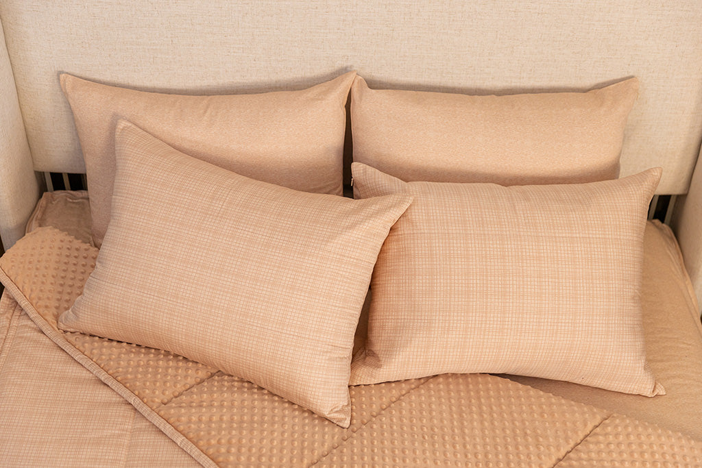 A bed made with peach pink zipper bedding with the comforter pulled back and pillows on top of the bed.