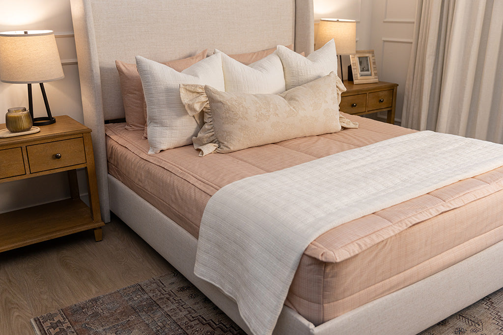 A bed made with peach pink zipper bedding and adorned with gray pattern and neutral pillows and blanket.