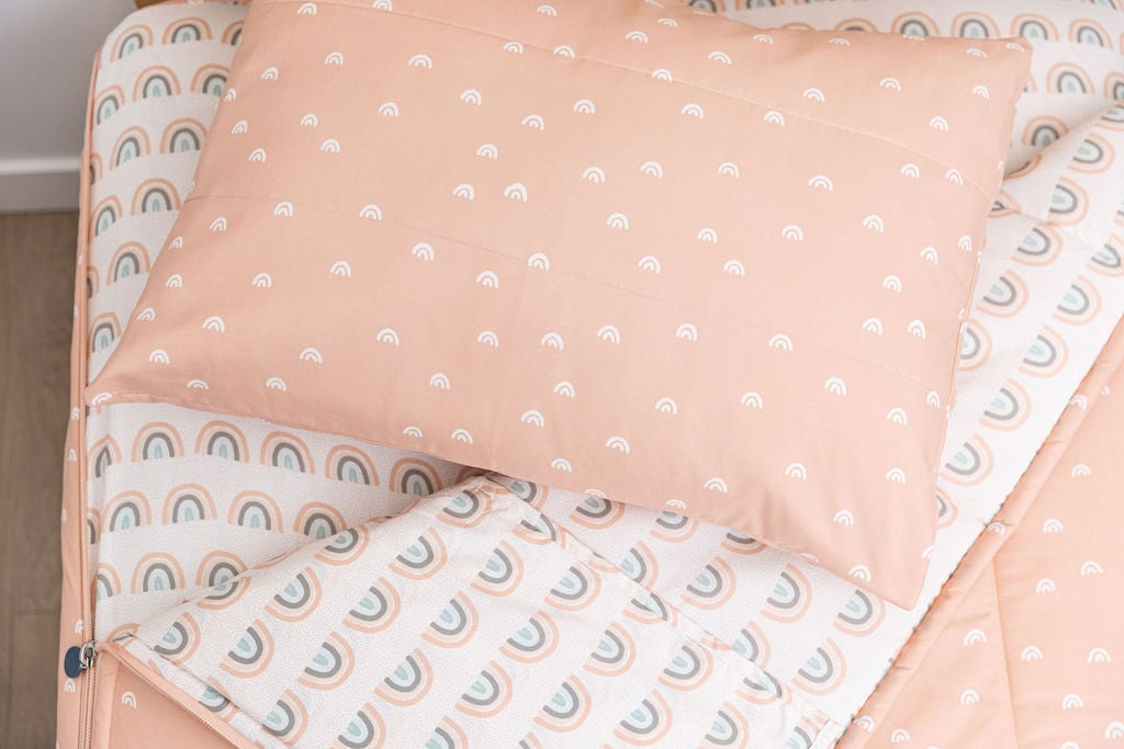 Peachy pink zipper bedding with small white rainbow pattern on the outside unzipped showing pastel rainbow sheet interior