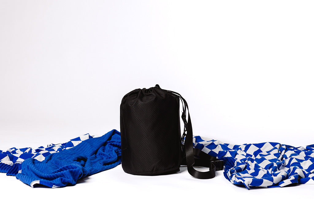 A white and blue check blanket next to a black bag on a white backdrop.