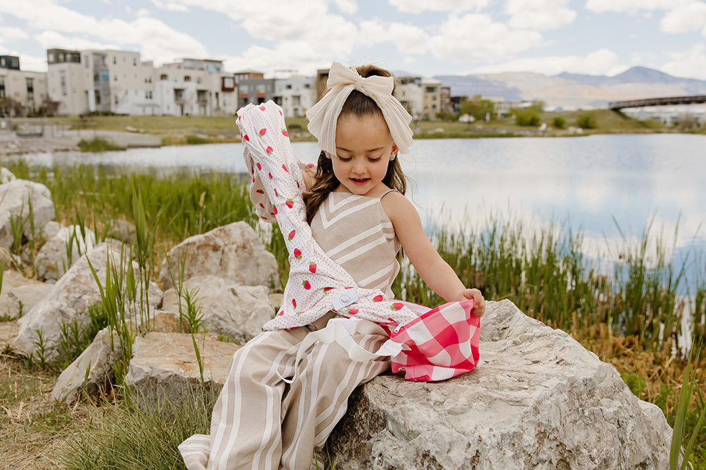 A little girl pulling her strawberry printed children's blanket out of the coordinating pink gingham bag.