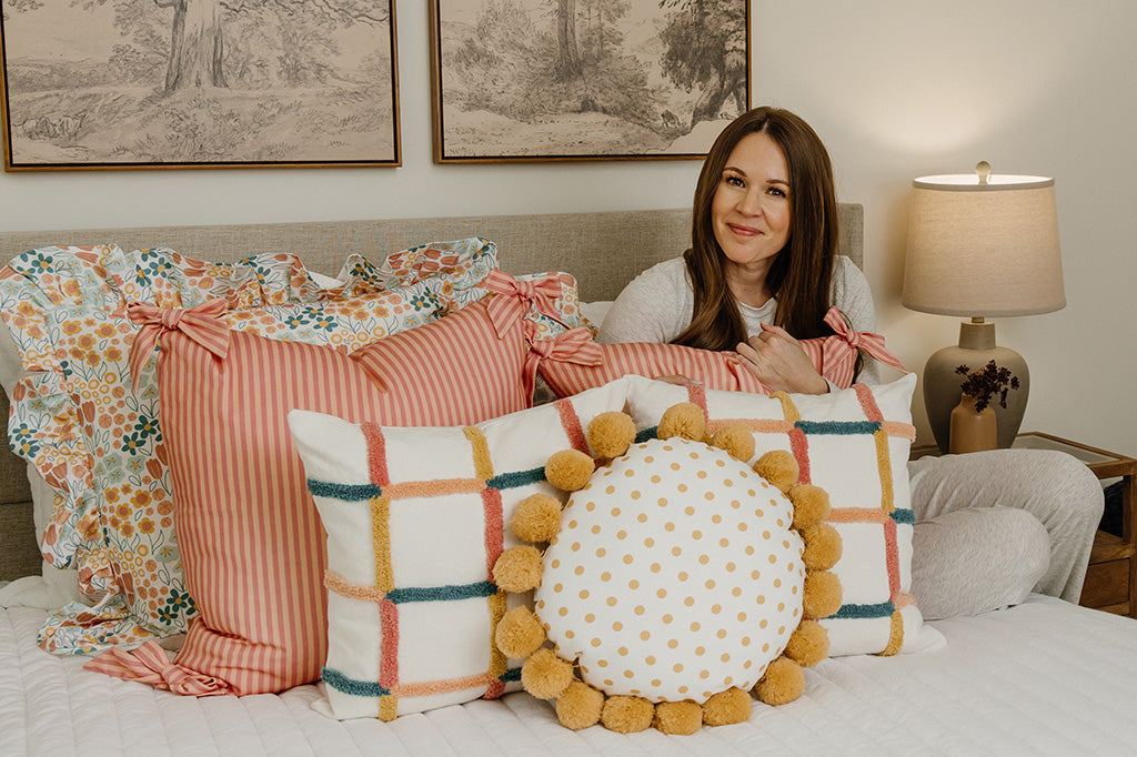 A woman snuggling multi-color and floral accessories on a white quilted bed.