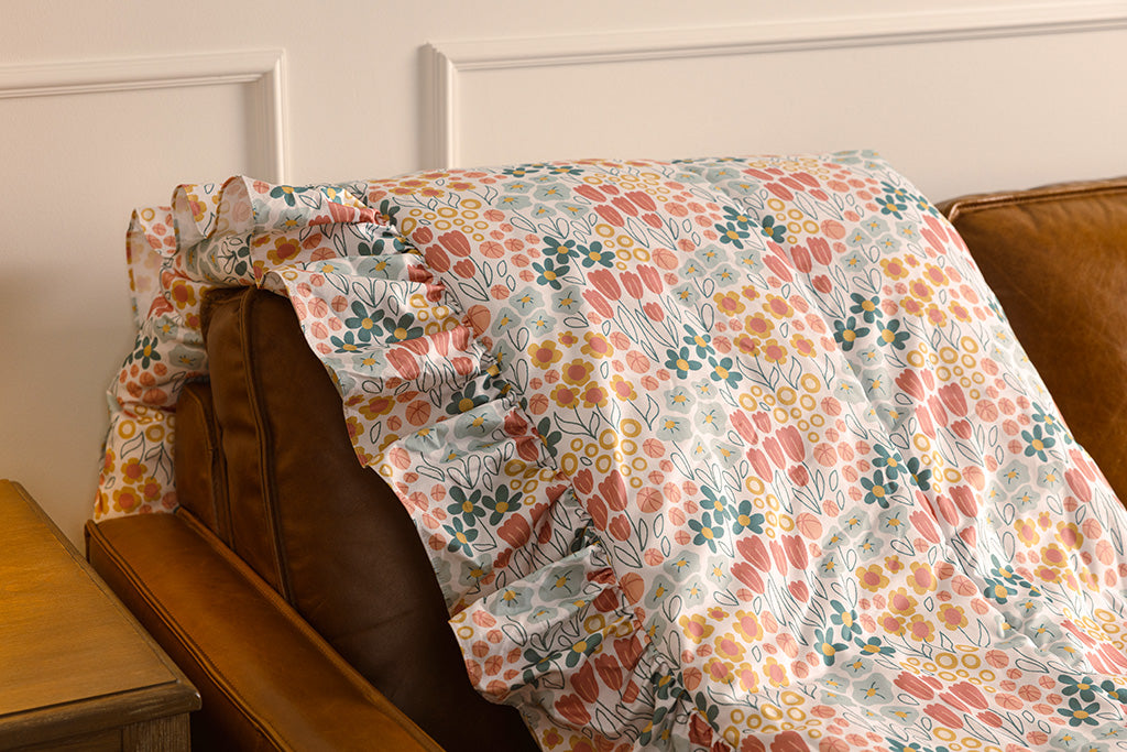 A multi-color floral print blanket with pink bubble minky on an orange leather couch.