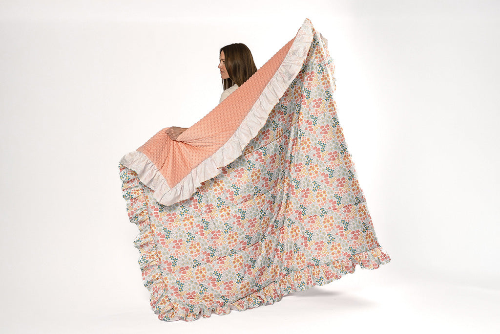 A woman holding a multi-color floral print blanket with pink bubble minky on a white backdrop.