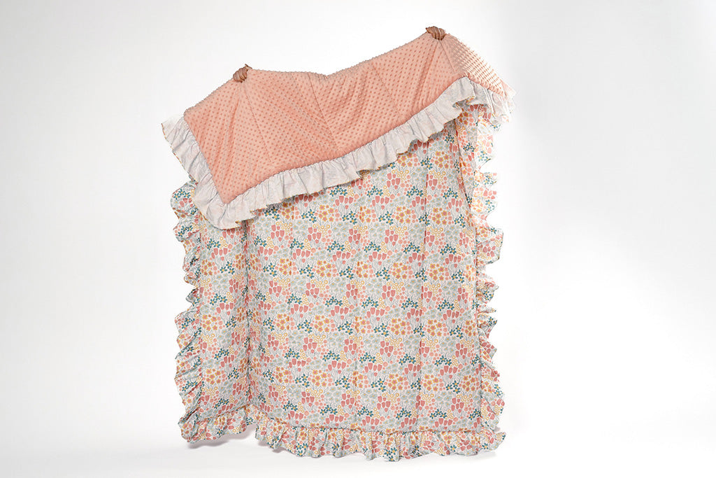 A woman holding a multi-color floral blanket with pink bubble minky on a white backdrop.