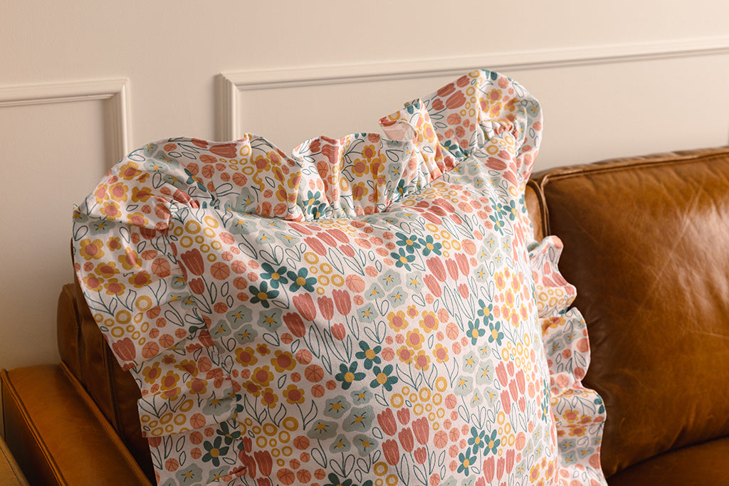 A multi-color floral pillow on an orange leather couch.