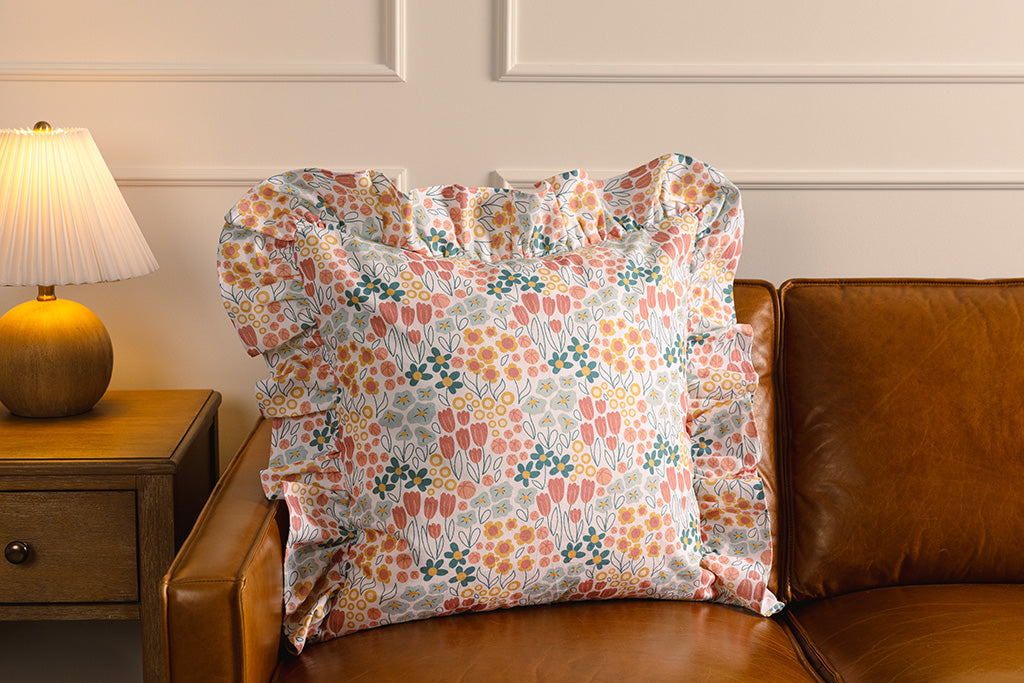 A multi-color floral pillow on an orange leather couch.