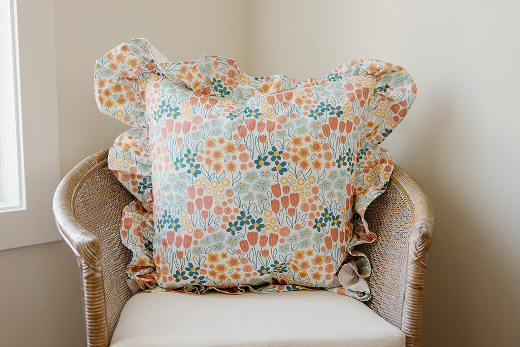 A multi-color floral pillow on a tan chair.