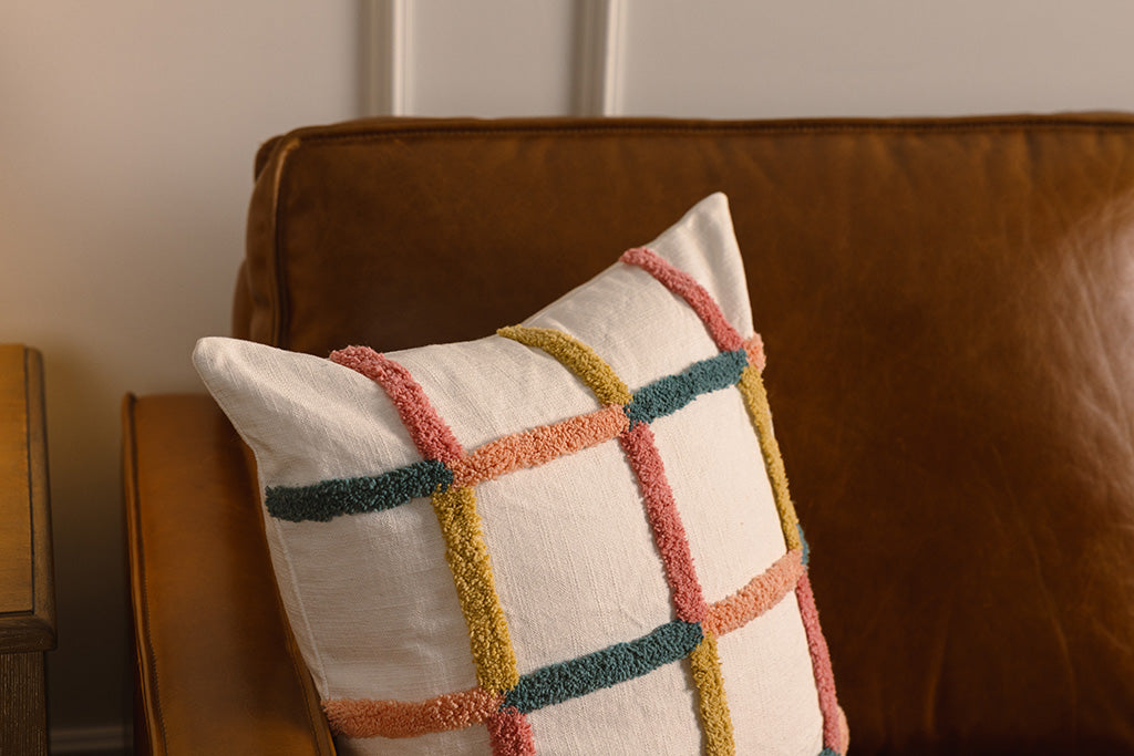 Multi-color grid pillow on an orange leather couch.