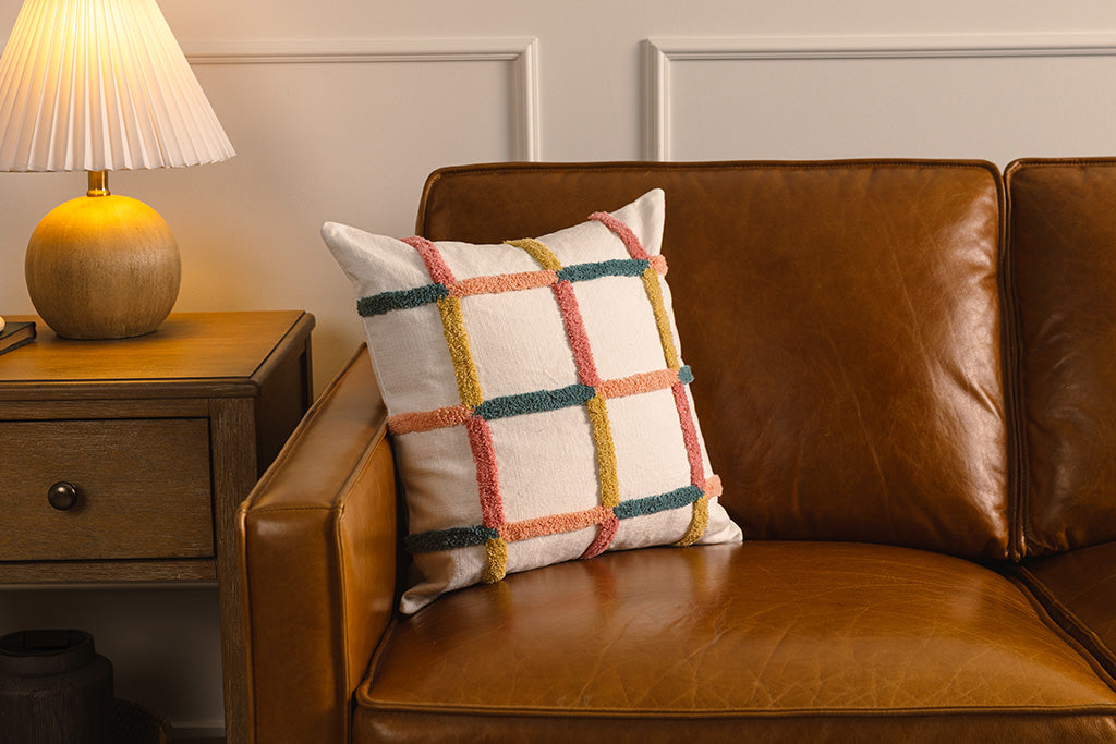Multi-color grid pillow on an orange leather couch.