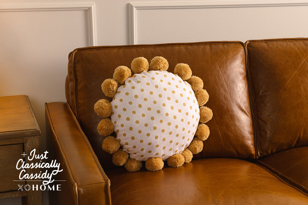 A white and yellow polkadot circular pillow on an orange leather couch.