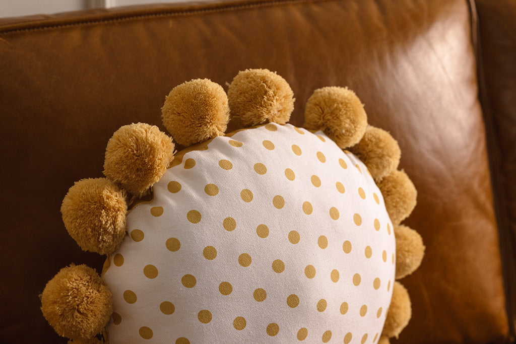 A white and yellow polkadot circular pillow on an orange leather couch.