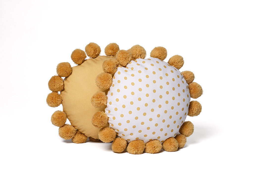 A yellow and white polkadot circular pillow on a white backdrop.
