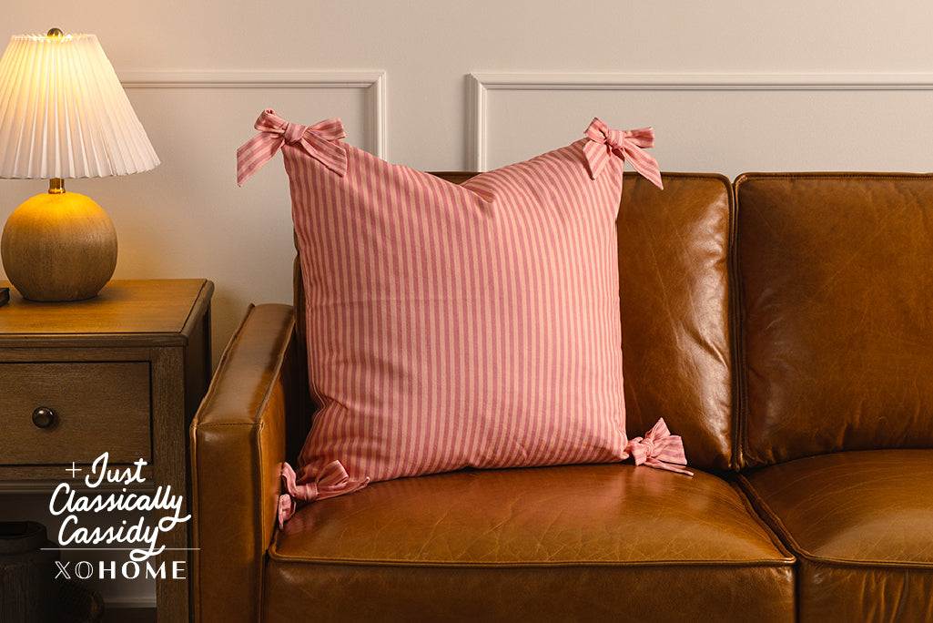 A soft pink on pink stripe pattern pillow on an orange leather couch.