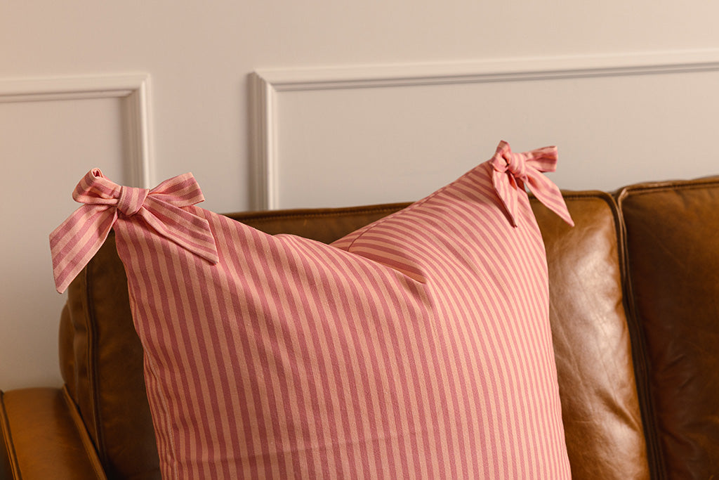 A soft pink on pink stripe pattern pillow on an orange leather couch.
