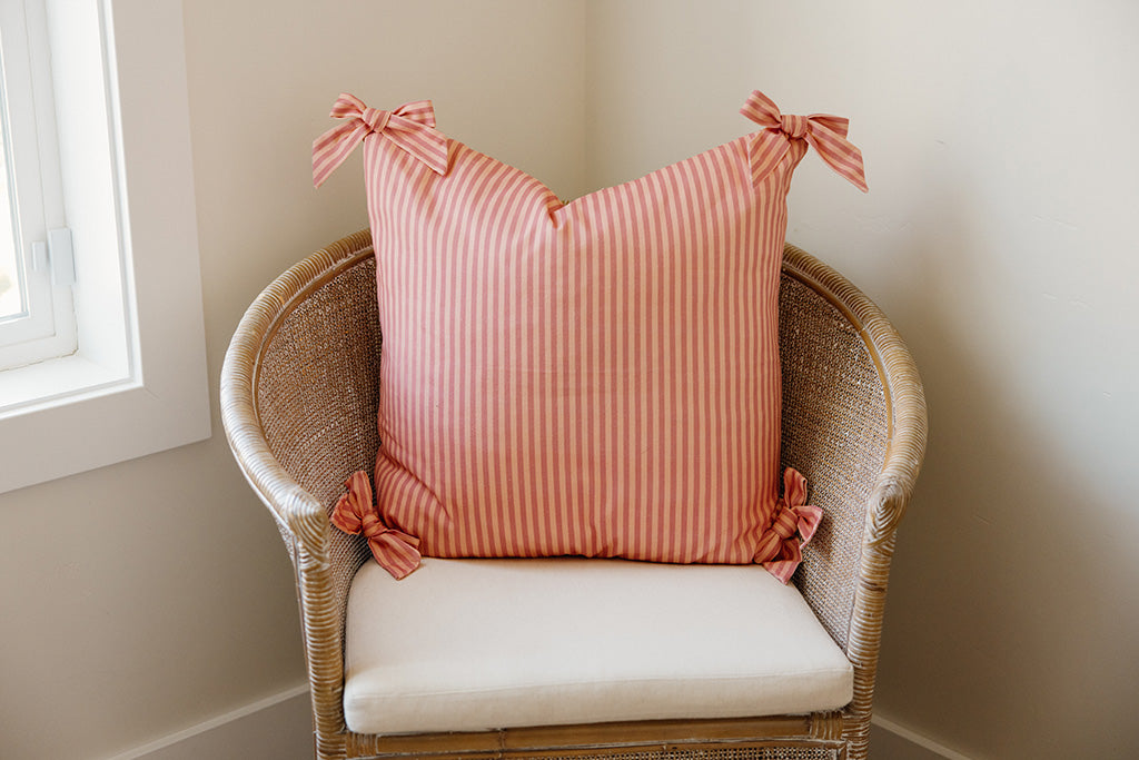 A soft pink on pink stripe pattern pillow on a tan chair.