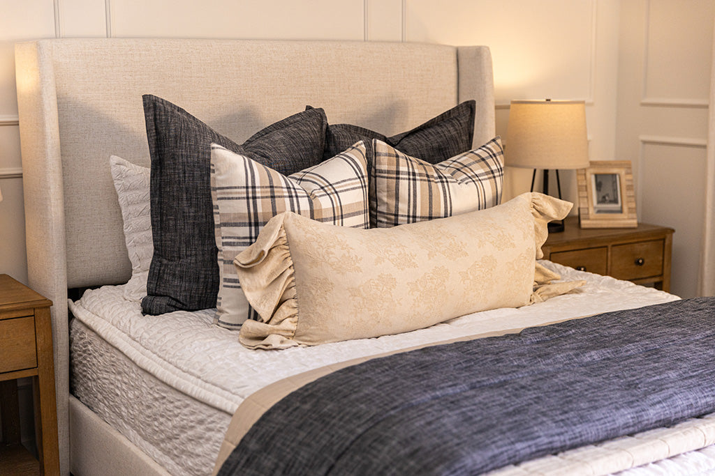 A brightly lit bedroom with a bed made with seersucker white zipper bedding and an assortment of neutral pillows and blankets.