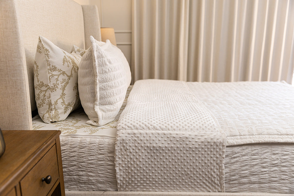 A side view of a bed made with seersucker white zipper bedding with the top unzipped halfway down the bed and the comforter folded down.