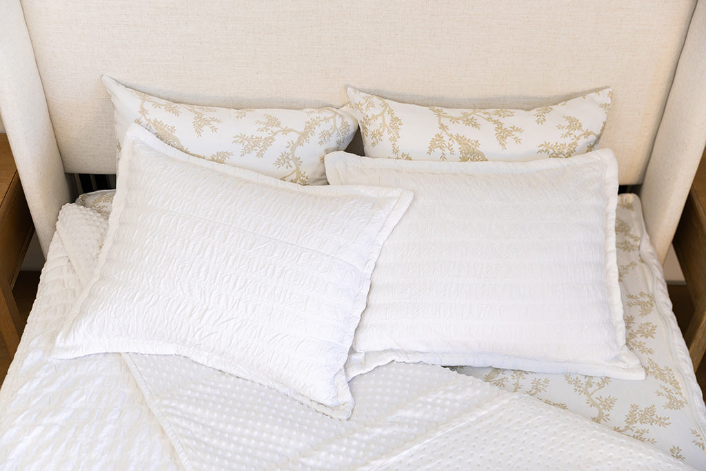 A bed made with seersucker white zipper bedding with the comforter pulled back and pillows on top of the bed.