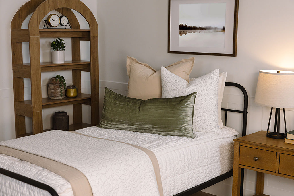 A twin bed made with seersucker white zipper bedding, decorated with neutral and green pillows and throw blankets.