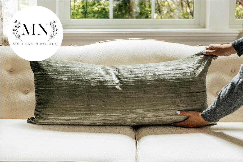 A woman placing a green XL velvet lumbar pillow on a cream antique couch.
