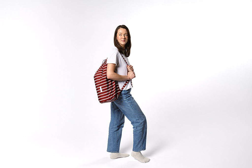 A woman holding her maroon and white striped stadium blanket bag on a white backdrop.
