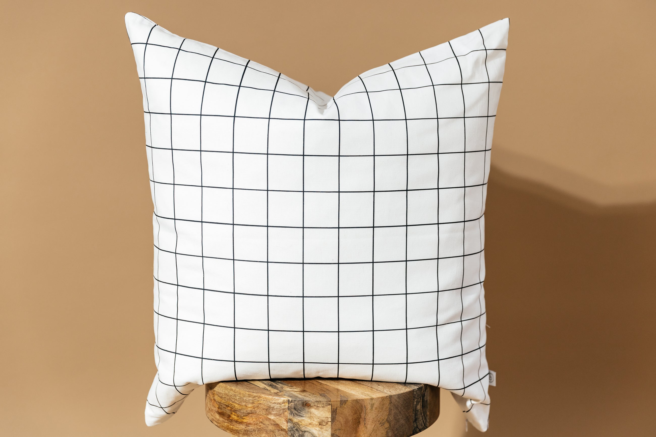 A white euro pillow with a black grid pattern arranged on a wood stool with a brown background.