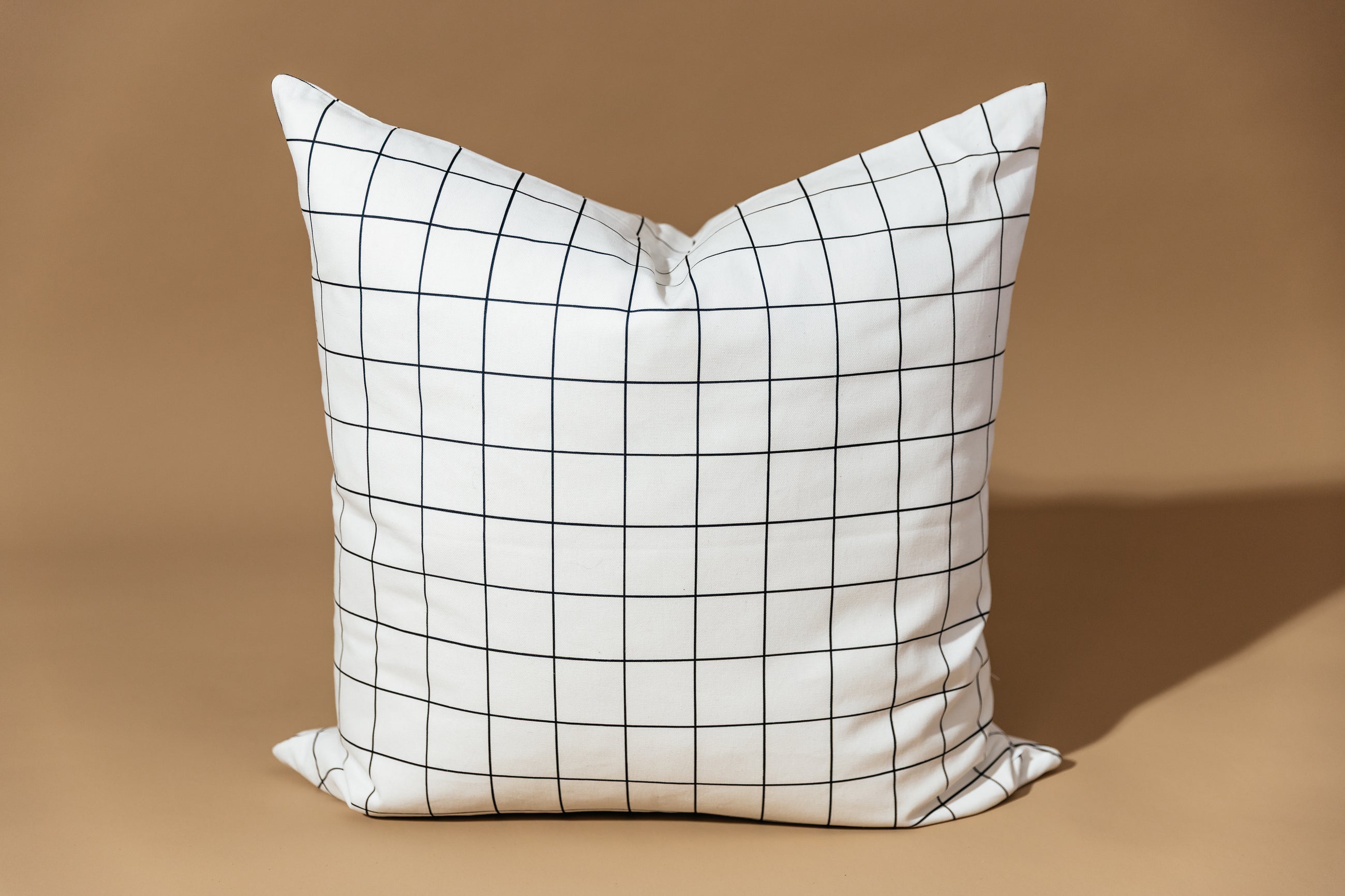 A white euro pillow with a black grid pattern arranged on a brown background.