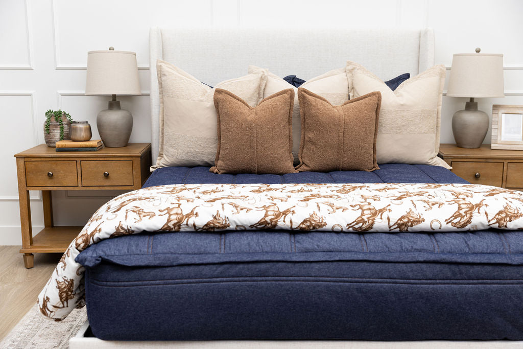 A bed made with dark denim blue zipper bedding and an assortment of neutral pillows and a cowboy western printed blanket.