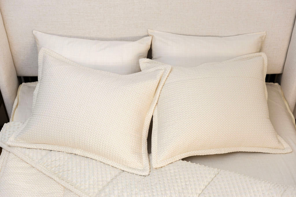 A bed made with cream waffle textured zipper bedding with the comforter pulled back showing minky interior lining and pillows on top of the bed.