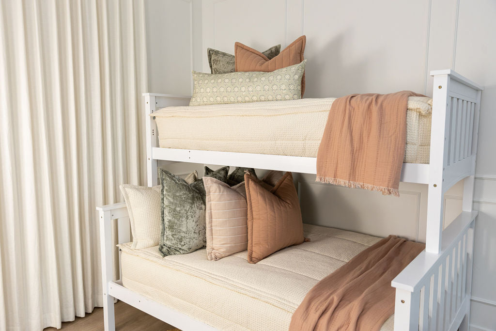 A standard bunk bed with both bunks made with cream waffle textured zipper bedding and neutral, green, and pink pillows and blankets.