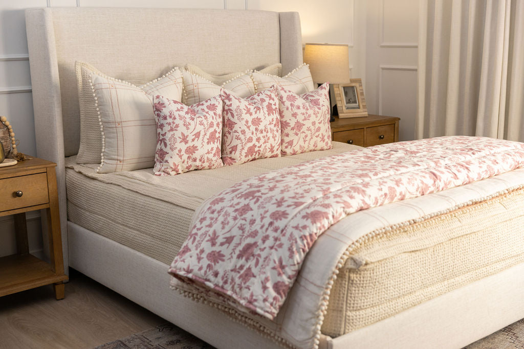 A brightly lit bedroom with a bed made with cream waffle textured zipper bedding an an assortment of green, terracotta pink, and floral pillows and blanket.