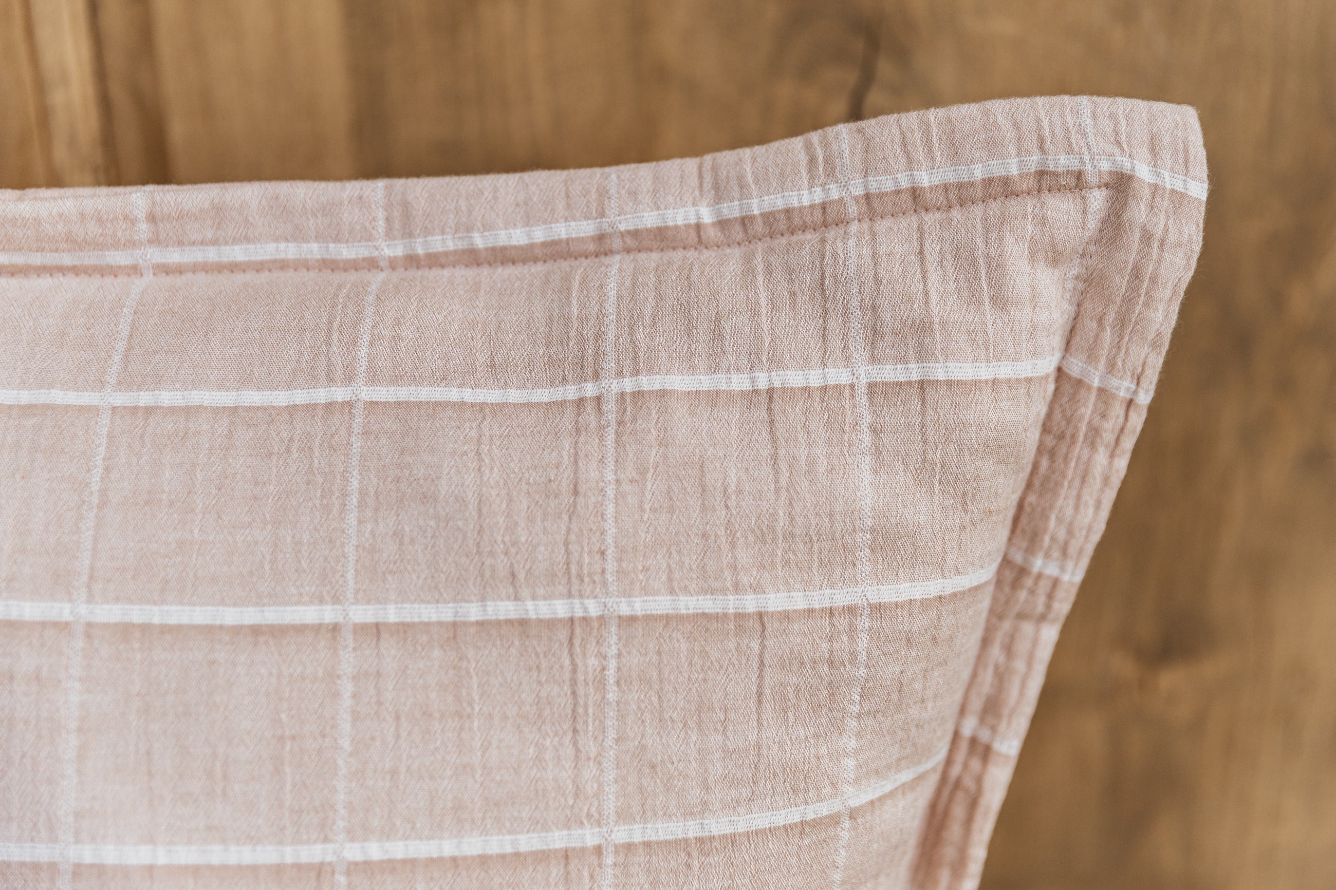 A close up corner view of a plaid terracotta euro pillow arranged on a brown background.