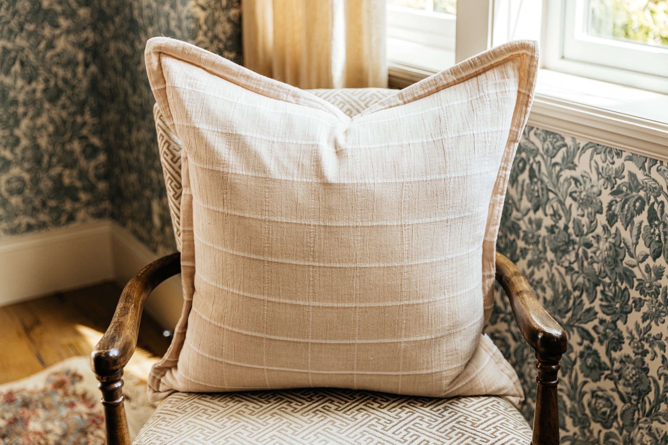 A plaid terracotta euro pillow arranged on an antique chair by a window.
