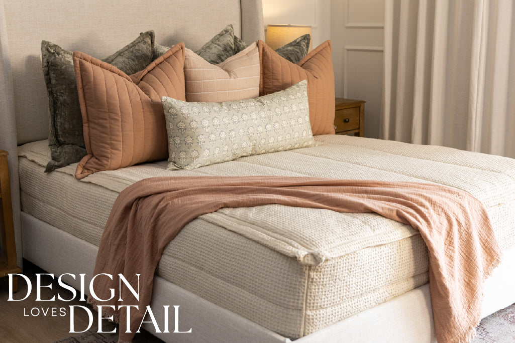 A bed made with cream waffle textured zipper bedding and an assortment of neutral green and pink throw pillows and blanket.