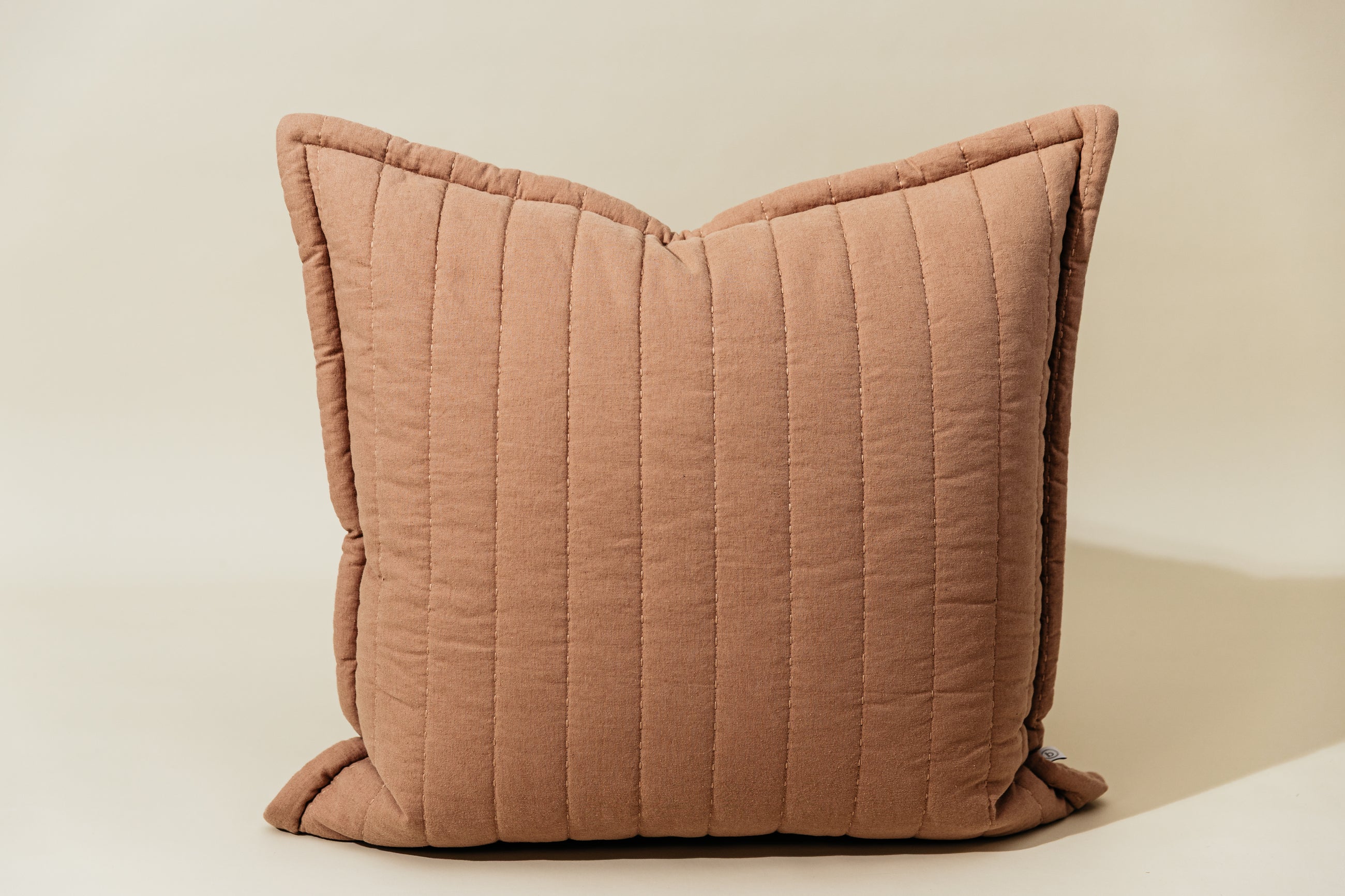 A terracotta quilted pillow arranged on a cream background.