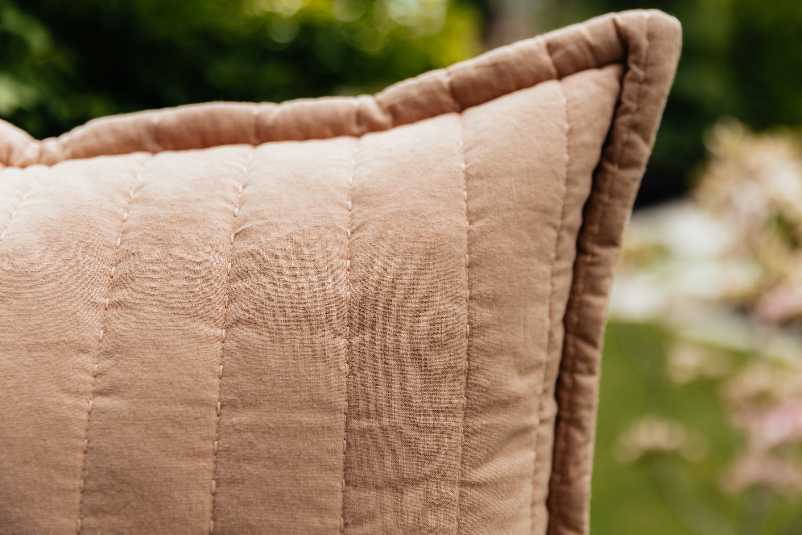 A close up corner view of a terracotta quilted pillow.