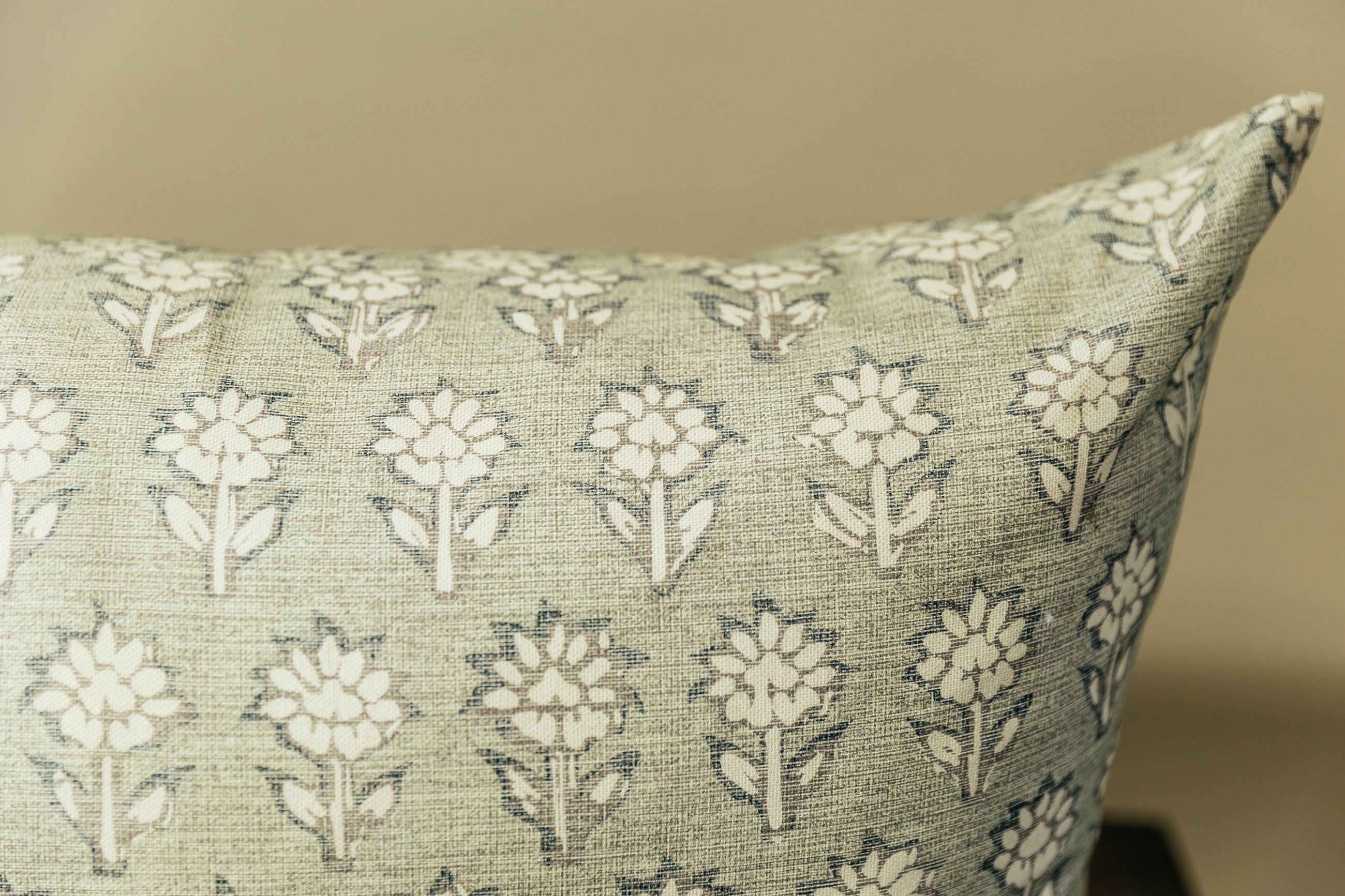 A close up corner view of a sage green and blue floral pattern XL lumbar pillow arranged on a bench with a light green background.